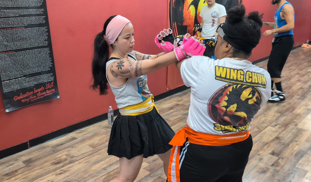 Woman in pink gloves practicing a close-range Wing Chun arm drill with a partner in a Tampa self-defense class