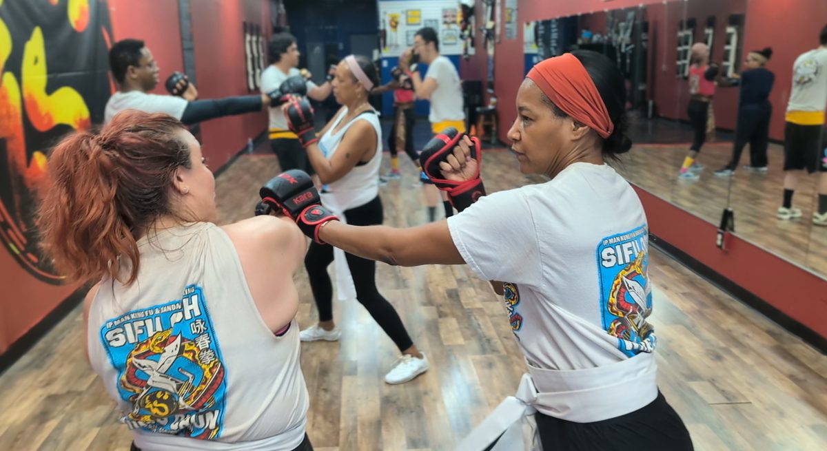 Two women practicing a gloved Wing Chun partner drill while other students train behind them at Tampa Wing Chun Kung Fu